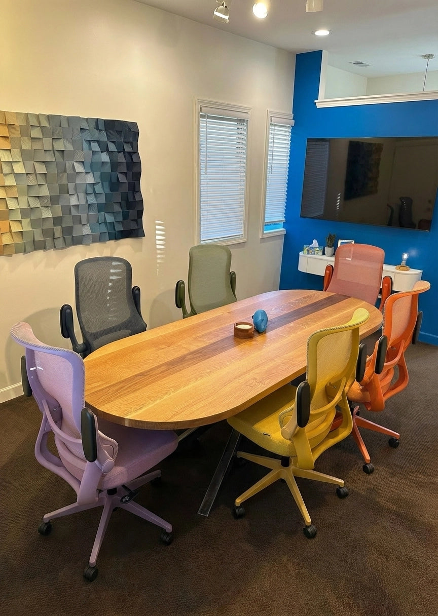 Six colorful Sunaofe ergonomic office chairs around a wooden oval meeting table in a modern workspace.
