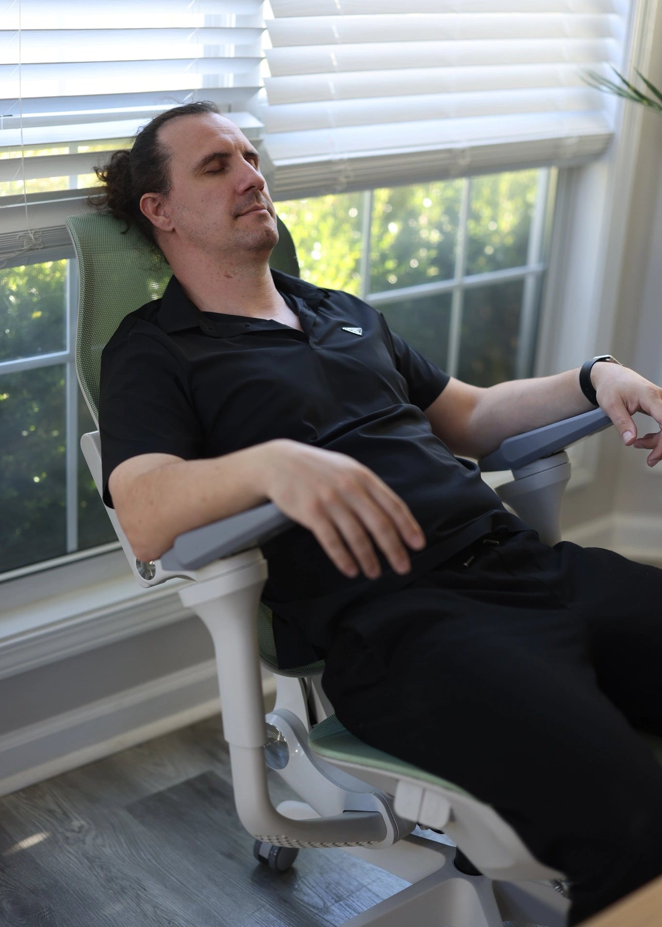 A man relaxes in a Sunaofe ergonomic mesh office chair featuring a comfortable reclining design by a sunlit window.