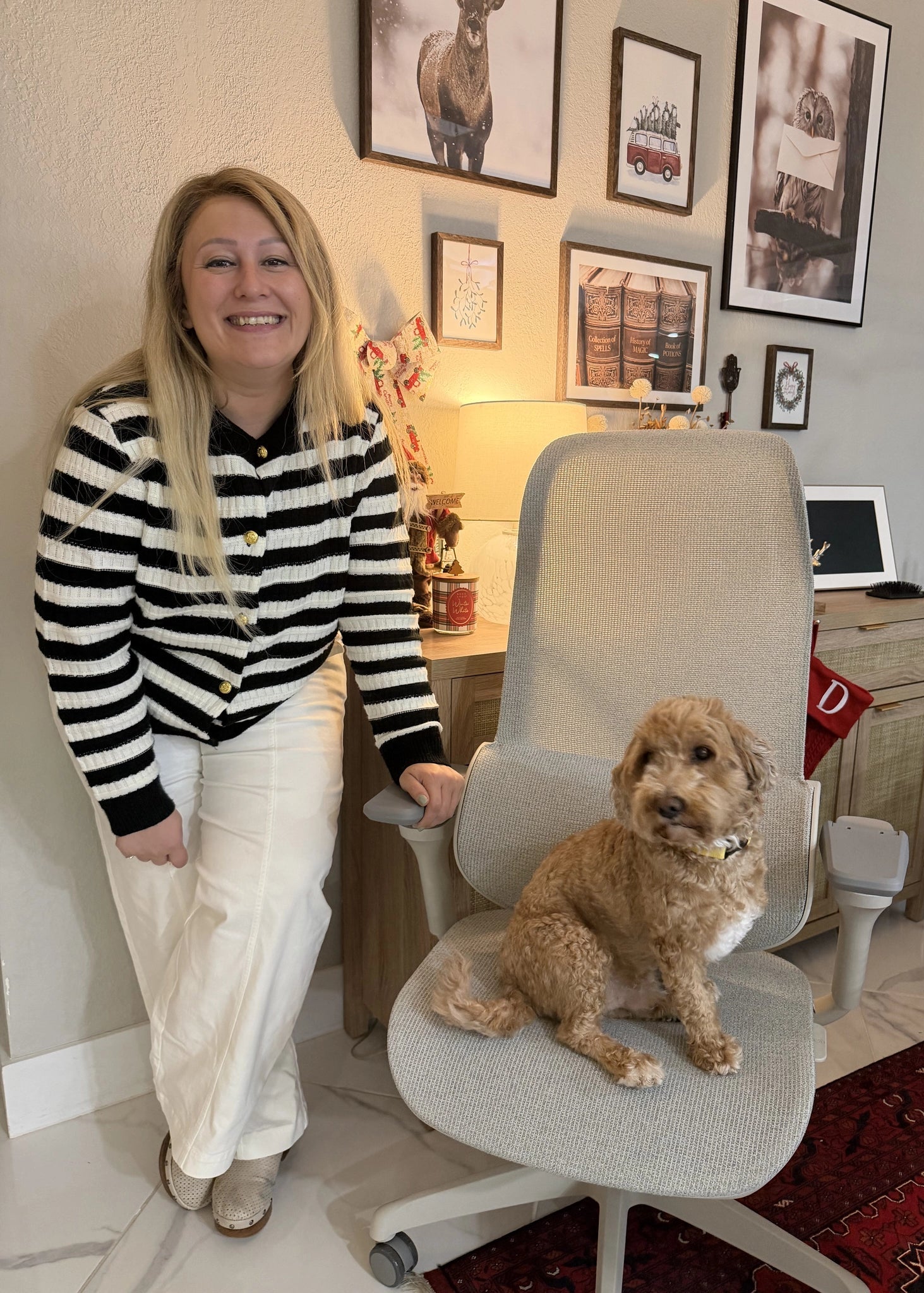 A woman smiling next to a Sunaofe ergonomic office chair with a small brown dog sitting on the seat in a home office.