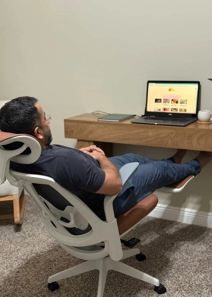 A man relaxes in a Sunaofe ergonomic office chair with his feet up in a comfortable home office setting.