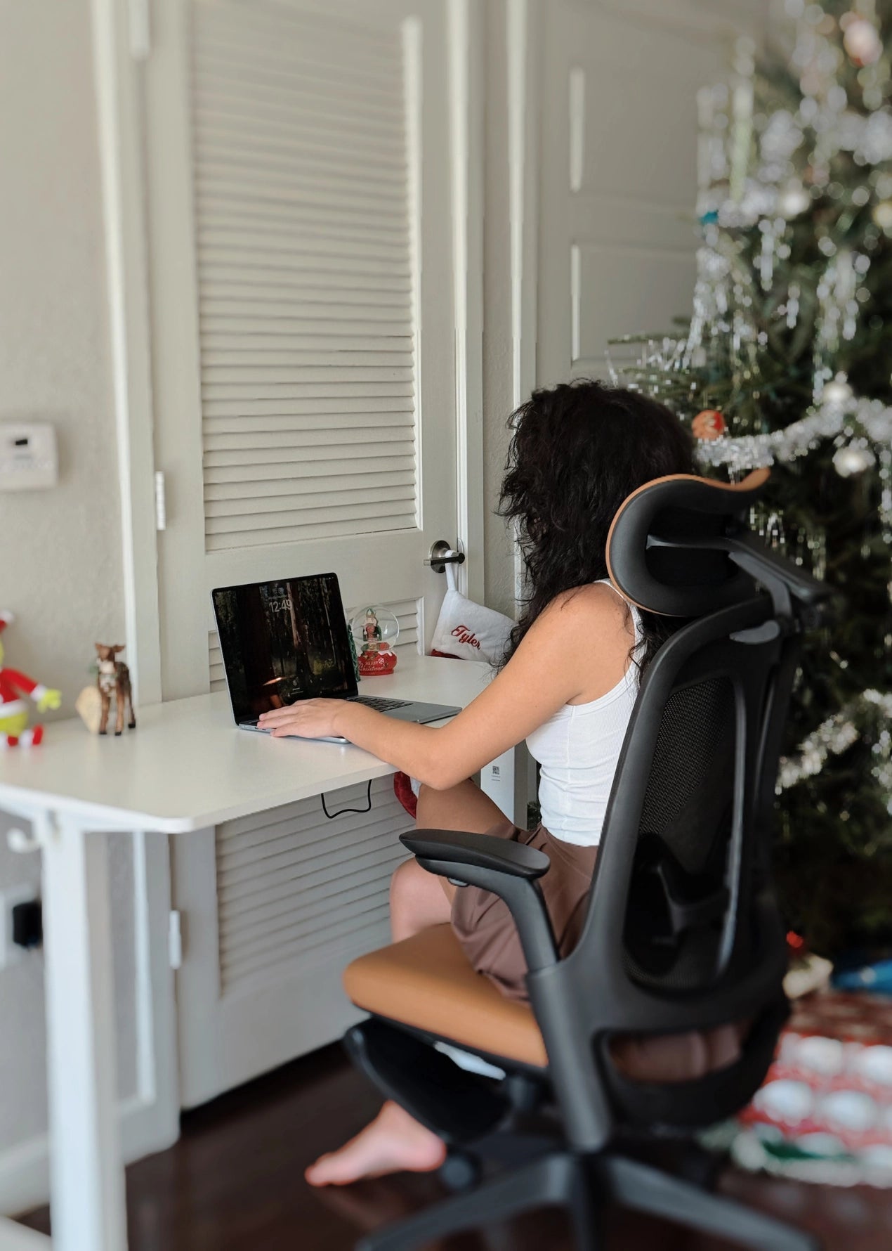 A person sits in a Sunaofe ergonomic office chair at a white standing desk in a festive home office setting.
