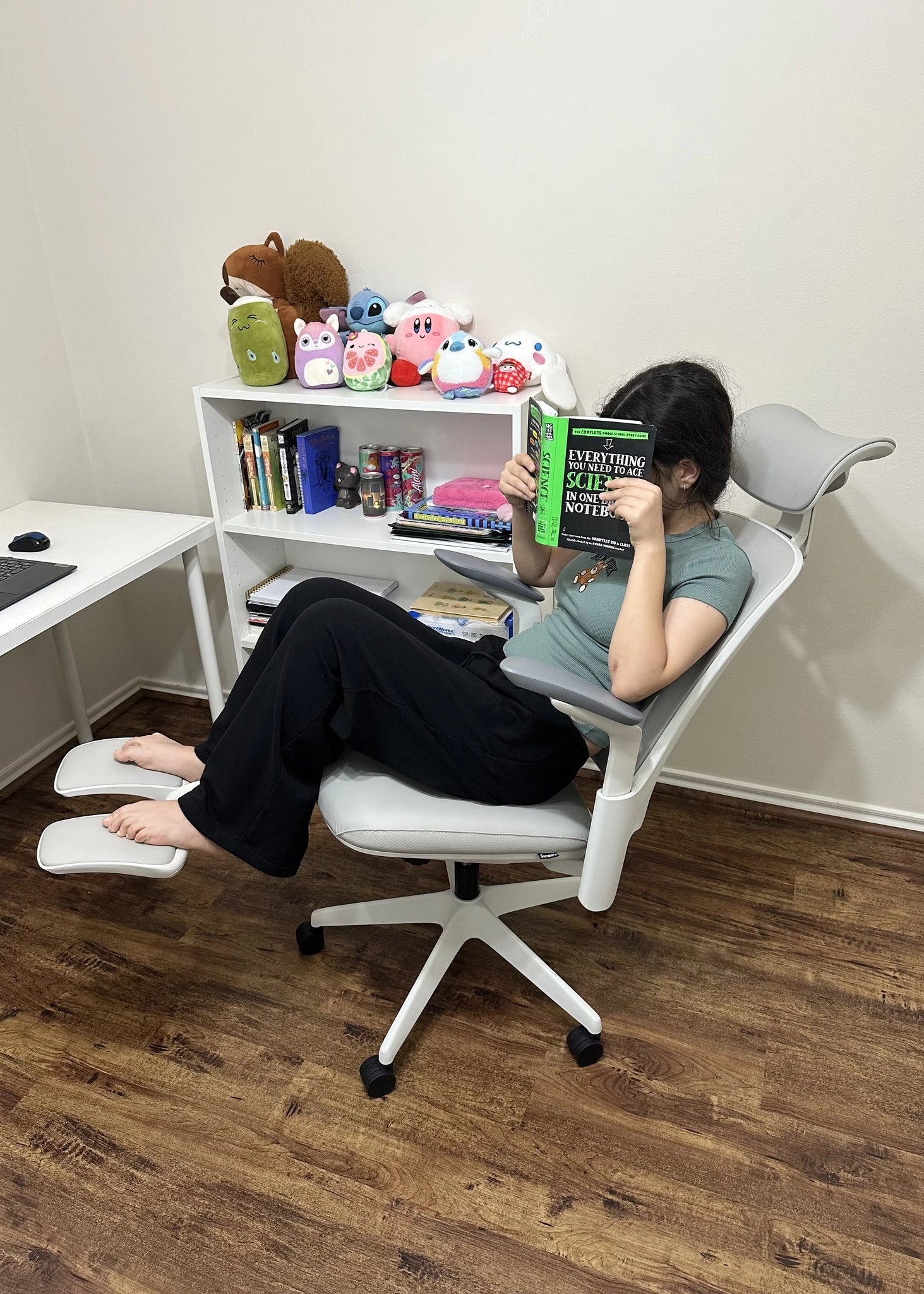 A person reading a book while reclining in a Sunaofe white ergonomic office chair with an extended footrest.