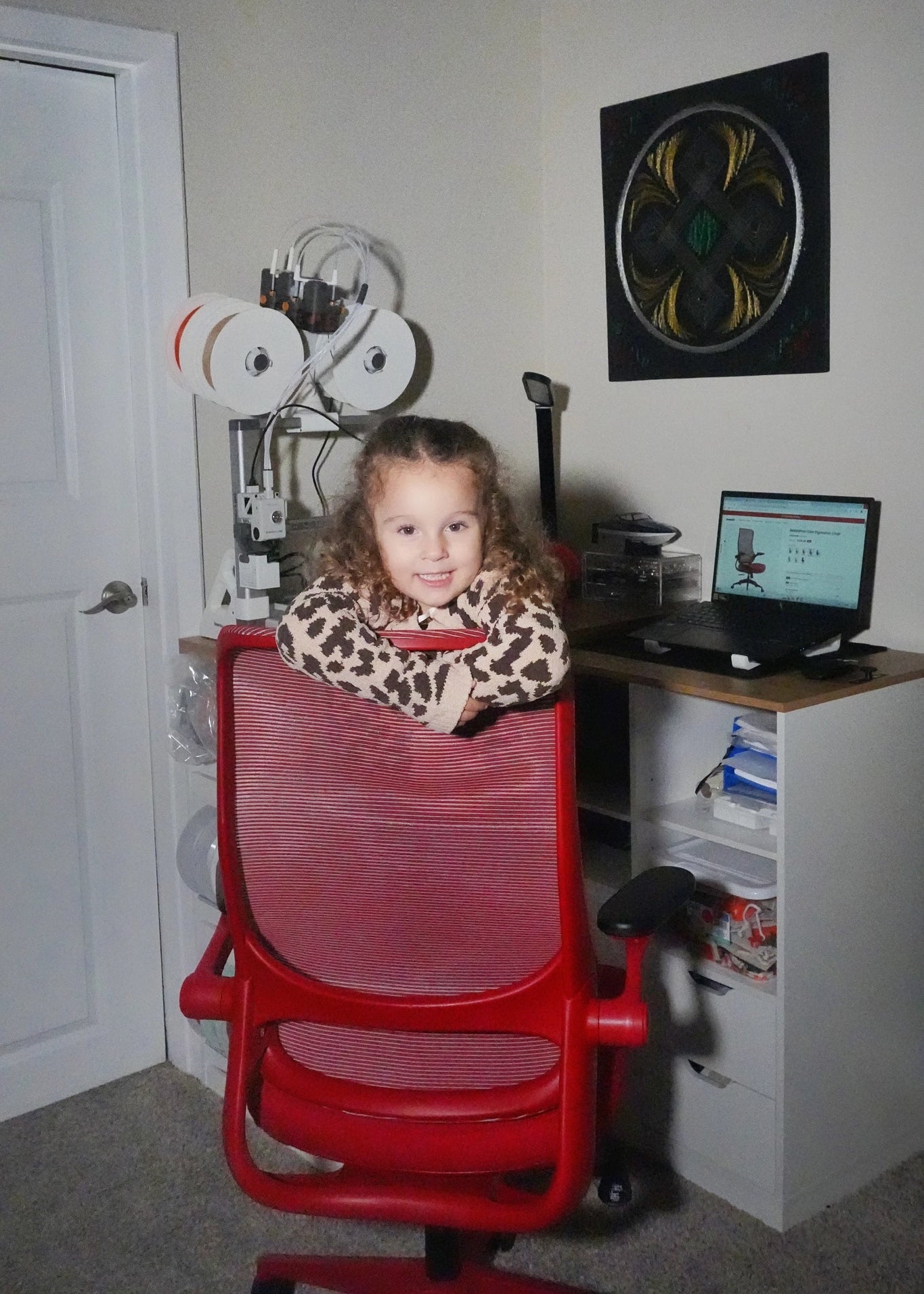 A young girl smiles behind a vibrant red Sunaofe ergonomic mesh office chair in a home workspace.