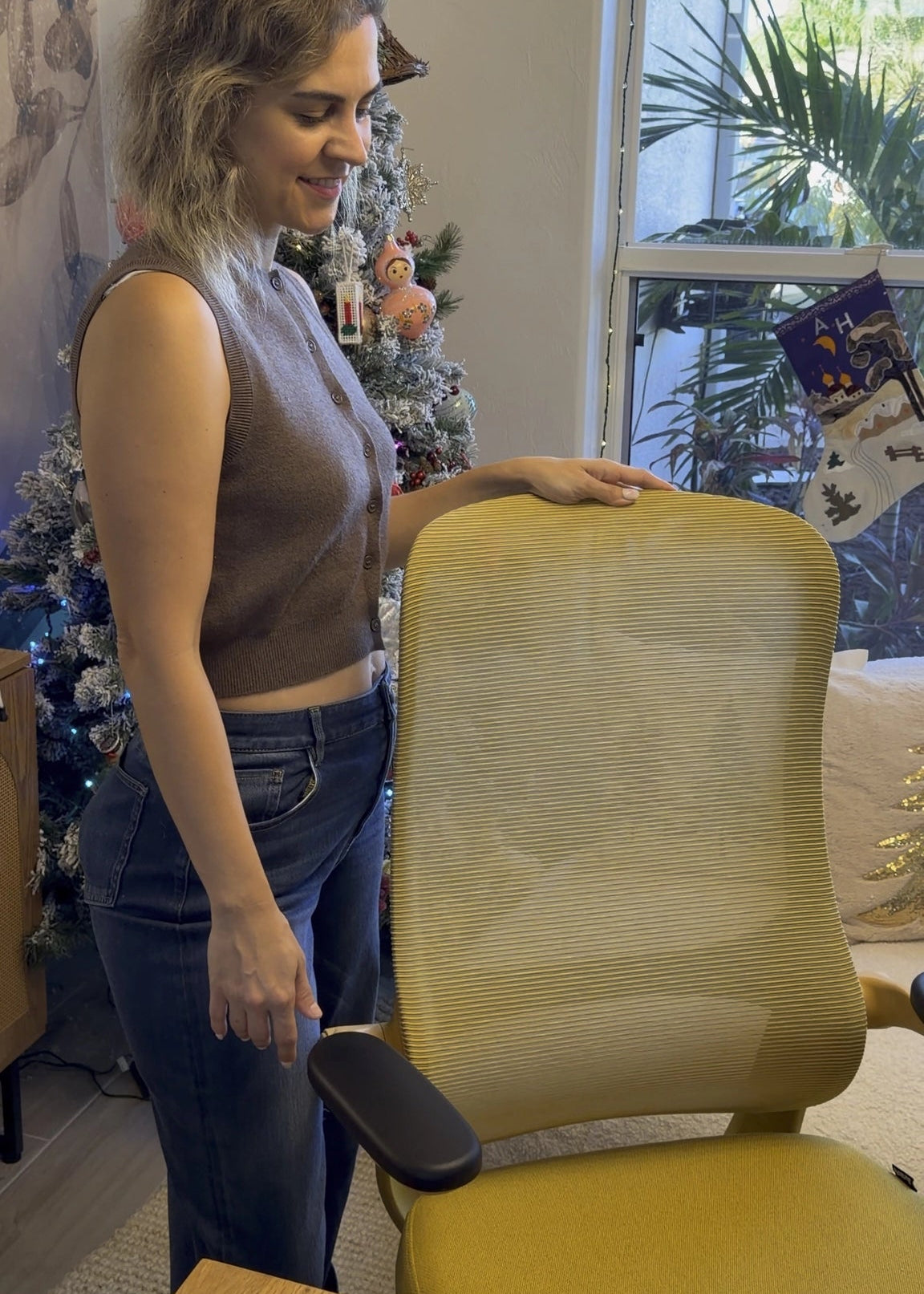 A woman smiling next to a vibrant yellow Sunaofe ergonomic mesh office chair in a cozy home office setting.