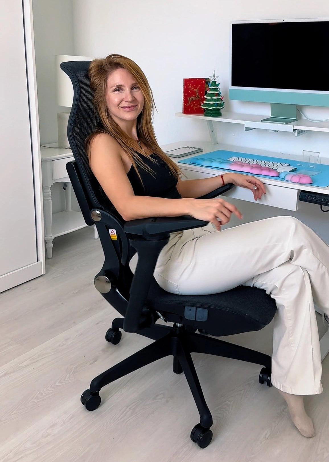A woman sits comfortably in a Sunaofe ergonomic mesh office chair at a modern white height-adjustable desk.