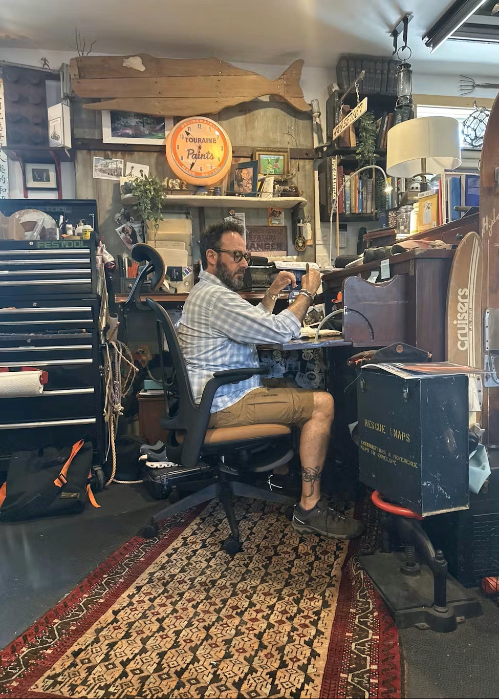 A man sits in a Sunaofe ergonomic office chair while working at a vintage desk in a creative workshop.