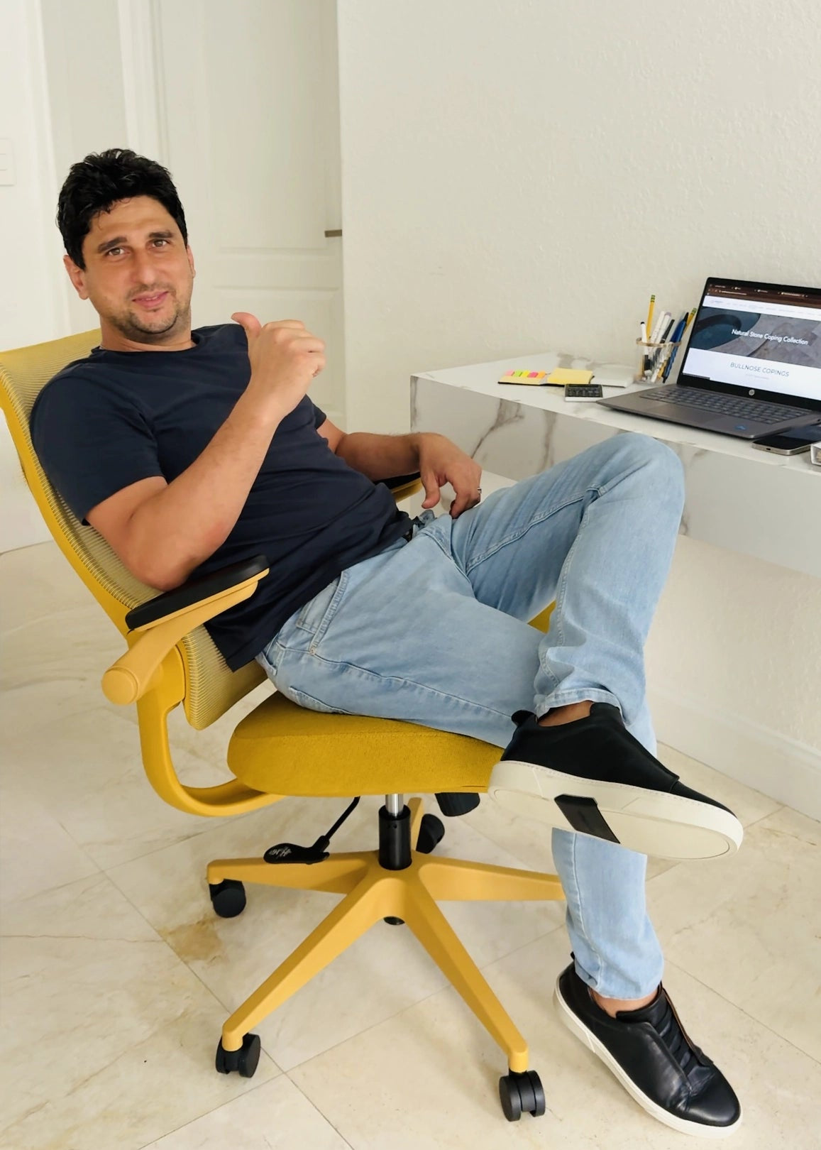 A man gives a thumbs up while sitting in a bright yellow Sunaofe ergonomic office chair in a modern home office.